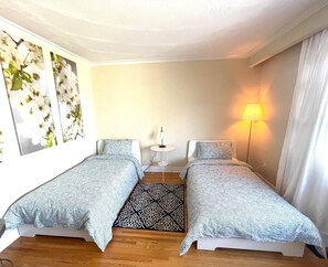 A bedroom with two single beds, a small round table, a floor lamp, and a patterned rug.