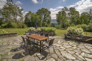 A patio with stone flooring, a wooden table, and metal chairs. - Mtn Views: Colonial Home on Kingdom Trails! (East Burke)
