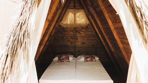 Ein Zimmer mit Holzbalkendecke und einem Bett mit weißer Bettwäsche und blumigen Kissen.