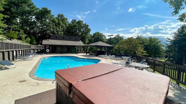 A swimming pool with lounge chairs and umbrellas, surrounded by trees and a building with a covered patio.
