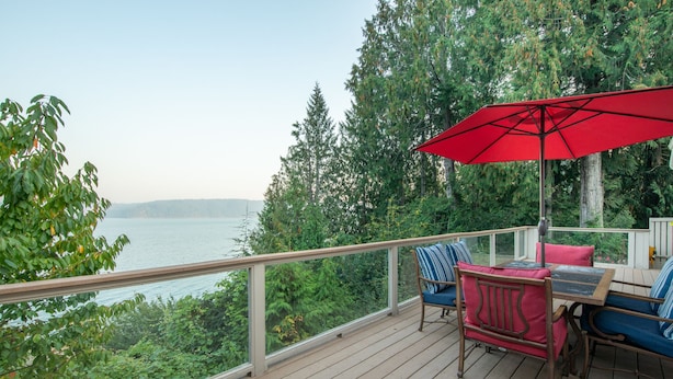 Une terrasse avec une table et des chaises, un parasol rouge et une vue sur l’eau.