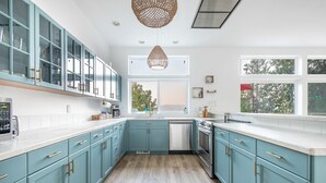 Une cuisine avec des armoires de couleur turquoise, un lave-vaisselle et une grande fenêtre donnant sur les arbres.