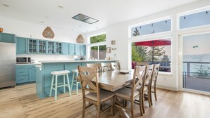 Une cuisine moderne avec des meubles de couleur turquoise, une table à manger en bois et une grande fenêtre donnant sur une terrasse.