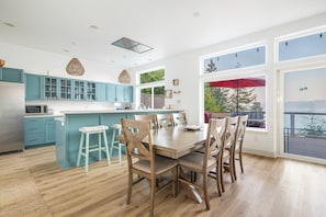 Une cuisine moderne avec des meubles de couleur turquoise, une table à manger en bois et une grande fenêtre donnant sur une terrasse.