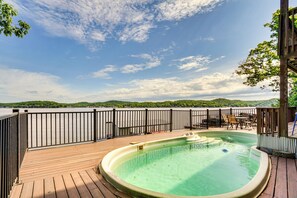 Un patio in legno con una vasca idromassaggio, mobili da esterno e vista su un lago e delle colline.