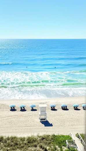 A beach with a row of umbrellas and chairs, a lifeguard tower, and a clear view of the ocean.