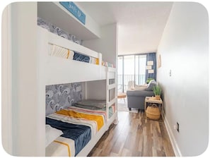 A bunk bed room with a sofa and a small table, a potted plant, and a view of the outdoors. - SunRay Suite - Beachfront condo with indoor and outdoor pool (Carolina Beach)