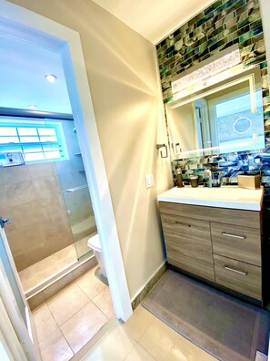 Un baño moderno con cabina de ducha de vidrio, tocador con espejo y salpicadero de azulejos.