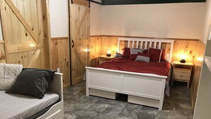 Un dormitorio con cama blanca, paredes de madera, un armario de madera y una mesita de noche con lámpara.