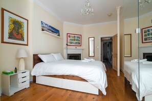 Quarto de hotel com uma cama grande, mesa de cabeceira com abajur, lareira e espelho.