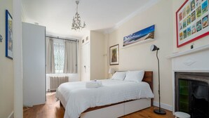 Un dormitorio con cama, radiador, chimenea, candelabro y ventana con cortinas.
