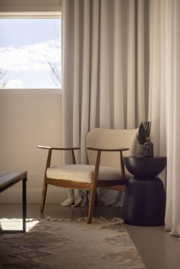 A modern room with a wooden chair, a small table, and a view of the outdoors through sheer curtains.