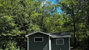 Eine kleine Holzhütte mit zwei Fenstern, einem Picknicktisch und einer Feuerstelle in einem bewaldeten Gebiet.