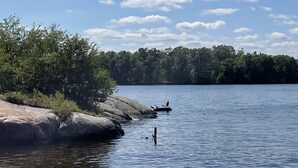 Ein ruhiger See mit blauem Himmel und bewaldetem Ufer.