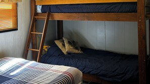 Ein Schlafzimmer mit Stockbett, einer Leiter, einem Fenster mit Vorhängen und einer gesteppten Bettdecke.