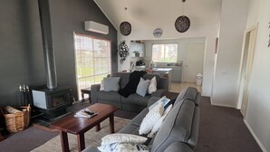 A modern living room with a grey sofa, a wooden coffee table, and a fireplace. - Cosy Pet Friendly Beach Cottage (Golden Beach)
