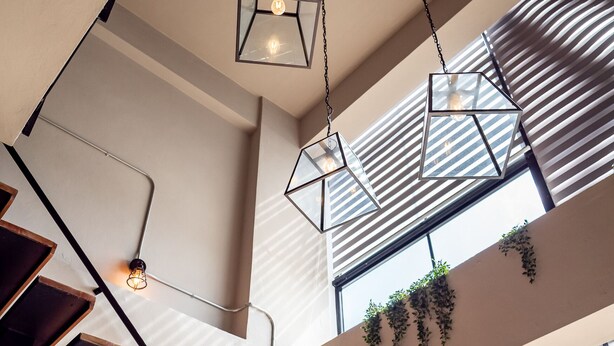 Een moderne trap met geometrische verlichtingsarmaturen en een uitzicht op de lucht door grote ramen.