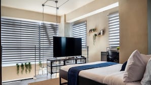 Een moderne slaapkamer met een bed, een televisie op een standaard, een bureau en een stoel.