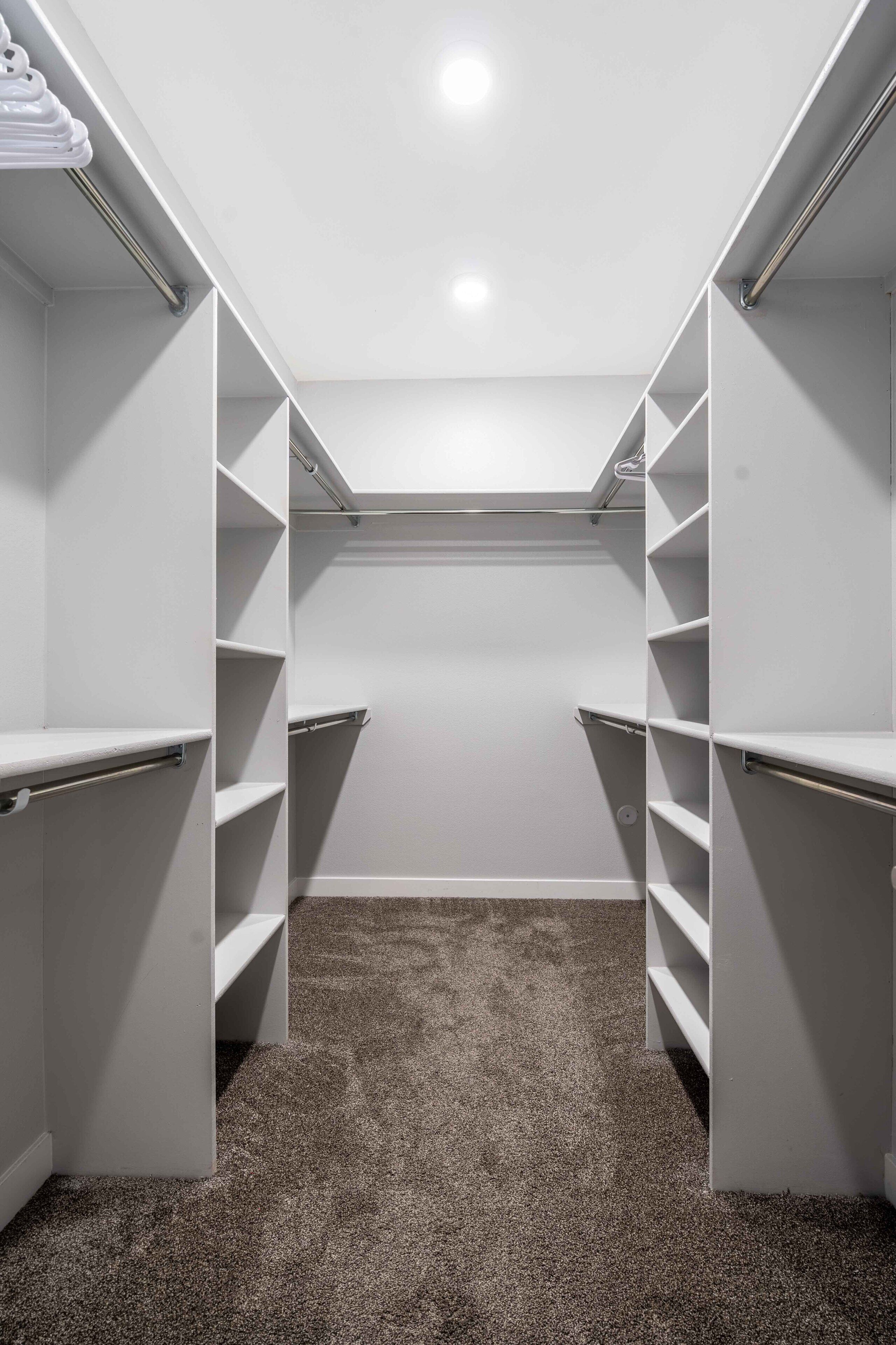 A walk-in closet with open shelving and a carpeted floor.