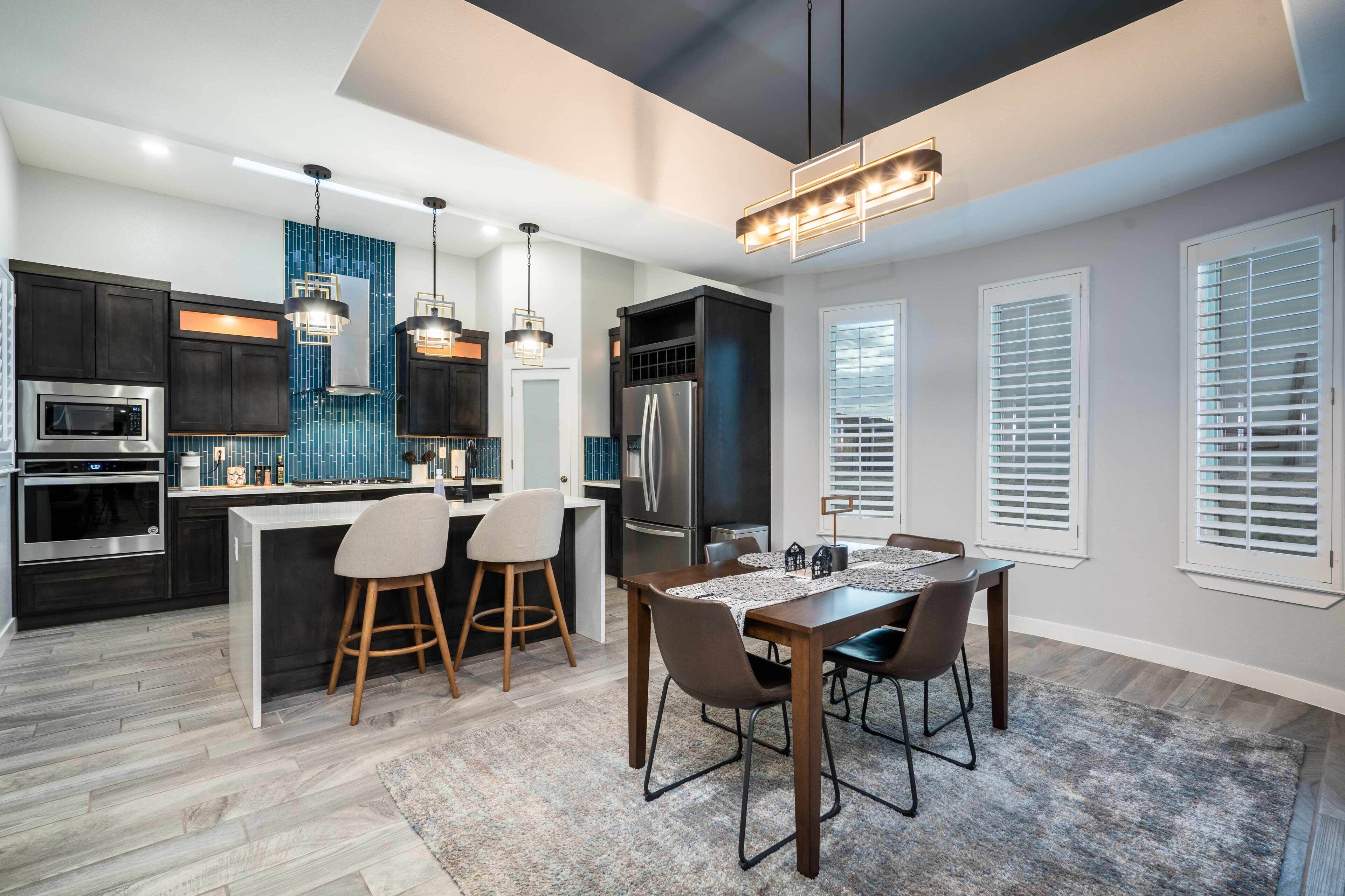 A modern kitchen with dark cabinets, a central island, bar stools, and pendant lighting.