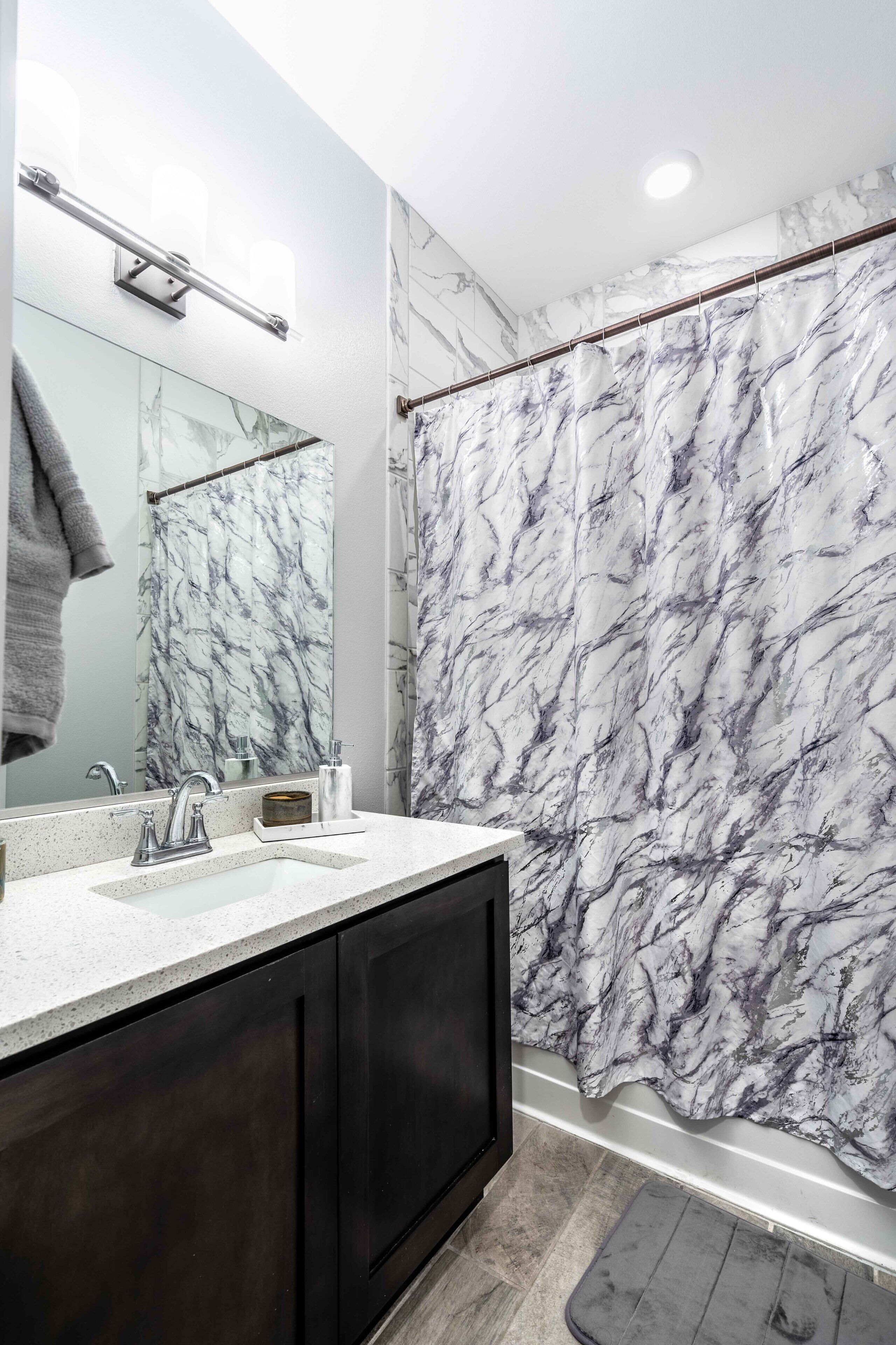 A bathroom with a marble shower curtain, a large mirror, and a dark wooden cabinet.