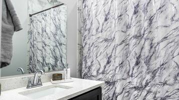 A bathroom with a marble shower curtain, a large mirror, and a dark wooden cabinet.