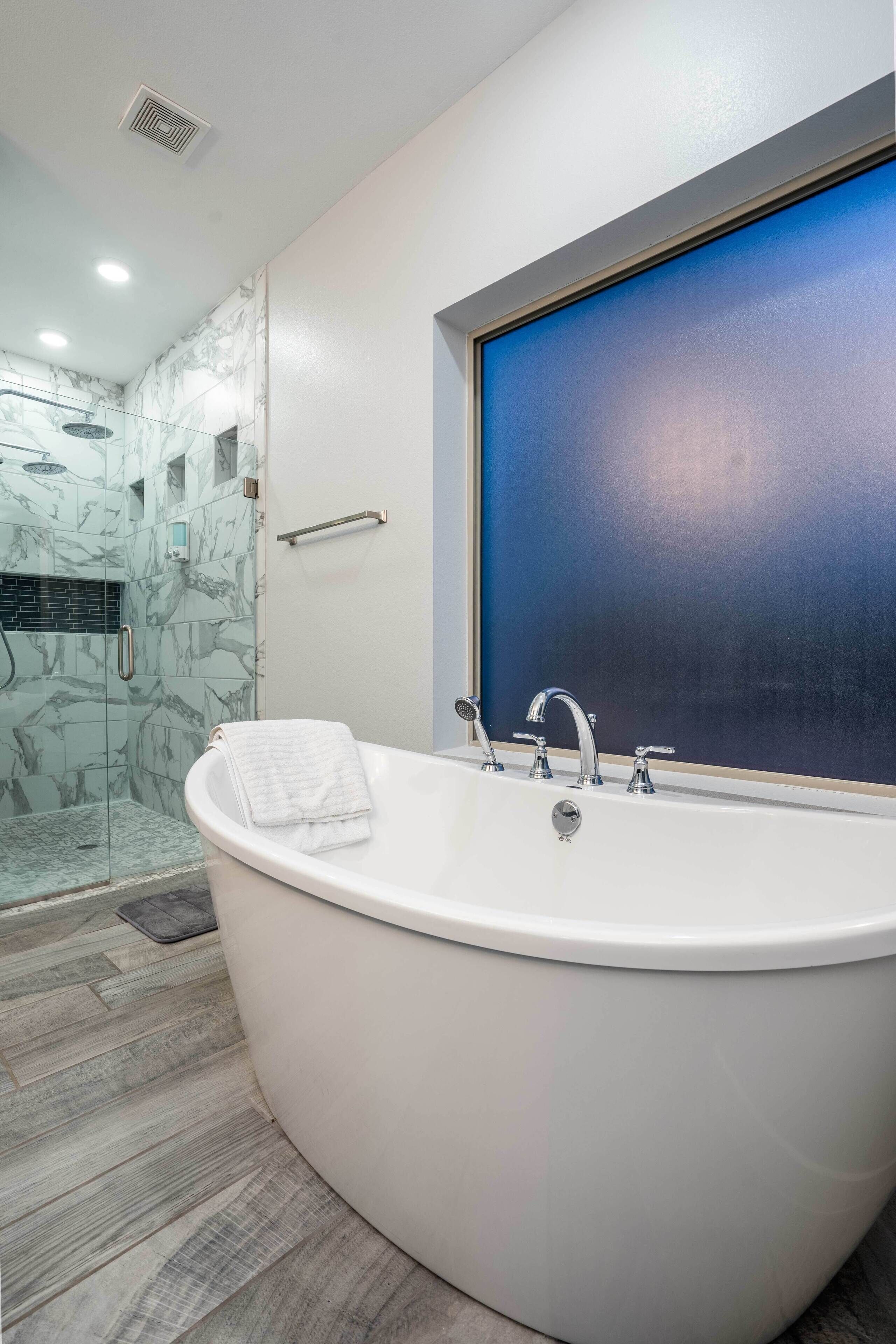 Un baño moderno con una bañera independiente, un box de ducha de vidrio y un ventanal amplio.