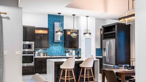 A modern kitchen with dark cabinetry, a blue backsplash, stainless steel appliances, and a central island with bar stools. - VILLA WITH MASTER SUITE CLOSE TO SHOPPING 4 BR 3BA (EL PASO)