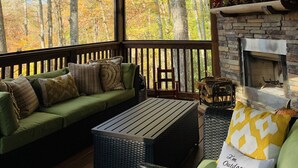 A covered outdoor seating area with a stone fireplace, wooden beams, and a view of autumn trees. - NEW High-Speed WiFi! Movie Theater, Pool Table & Hot Tub in Bear Lake Reserve!! (Tuckasegee)