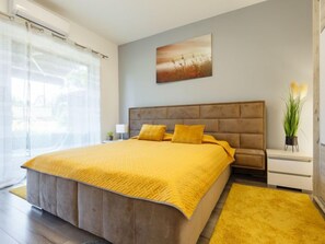 A modern bedroom with a large bed, a headboard, a bedside table, a nightstand, a window with curtains, and a painting on the wall. - Juventus by Interhome (Balatonföldvár)