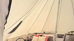 Una habitación con carpa, una cama, una mesita, una silla y un calentador.