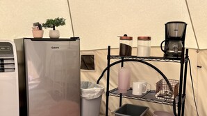 Un espacio habitable compacto con un refrigerador Galanz, una pequeña planta en maceta, una cafetera y una estantería con diversos objetos.