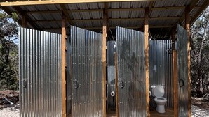 Un baño portátil con revestimiento de metal corrugado, vigas de madera de soporte y techo de tejas.