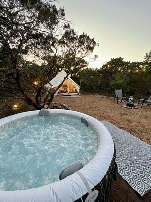 A hot tub surrounded by a wooden deck, a tent, and outdoor furniture.