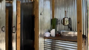 Un espacio al aire libre cubierto con un muro de lámina corrugada, vigas de madera y suelo de grava.