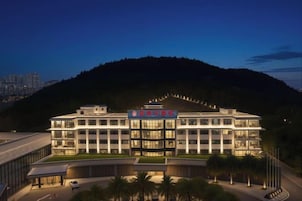 Un hotel de varios pisos con un diseño arquitectónico moderno, que cuenta con una entrada destacada y una zona ajardinada con palmeras.