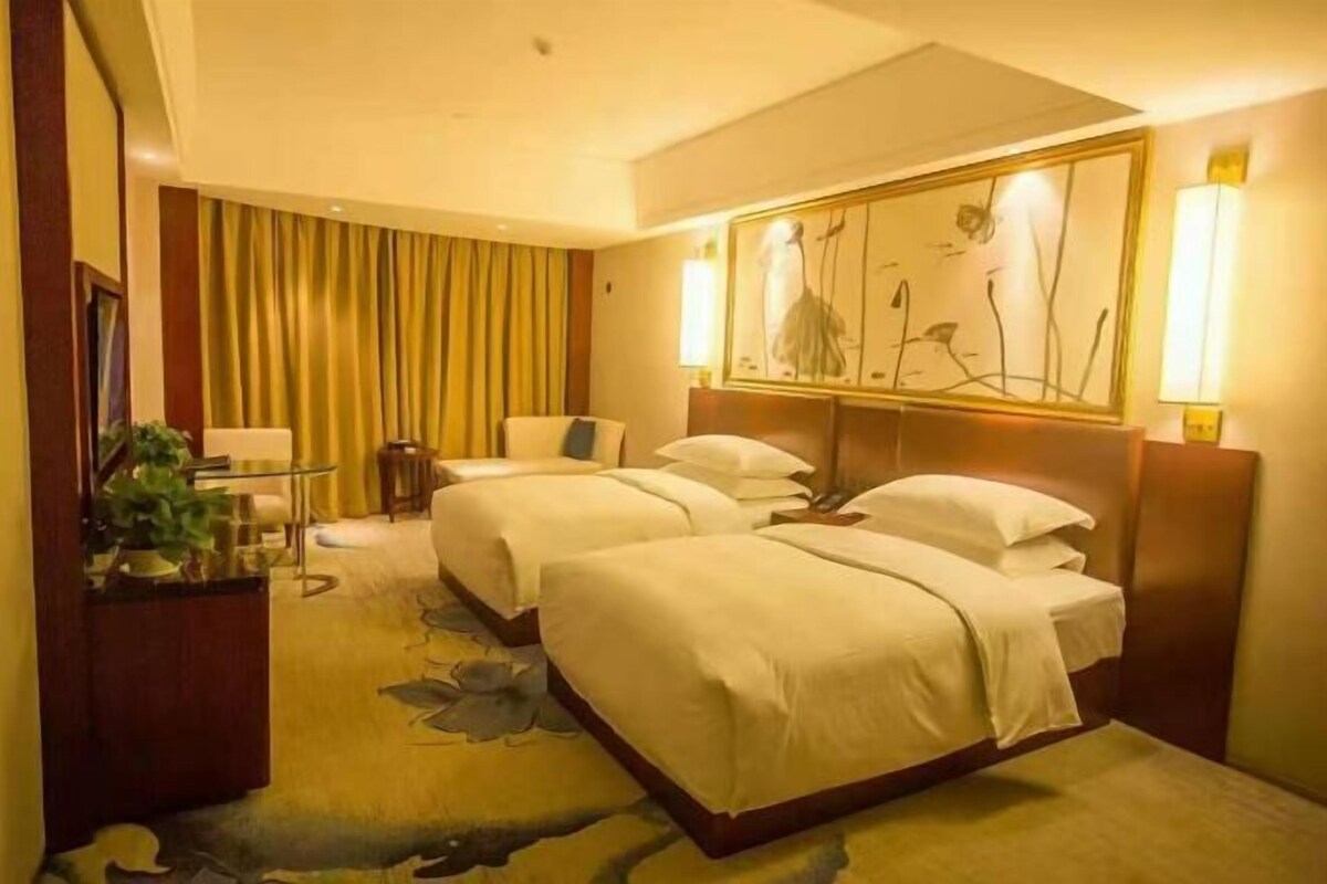 Habitación de hotel con dos camas, un escritorio, una silla y un cuadro grande en la pared.