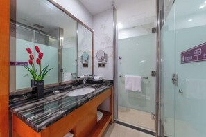 Un baño moderno con un lavabo de mármol, un espejo grande y una ducha con mampara de vidrio.