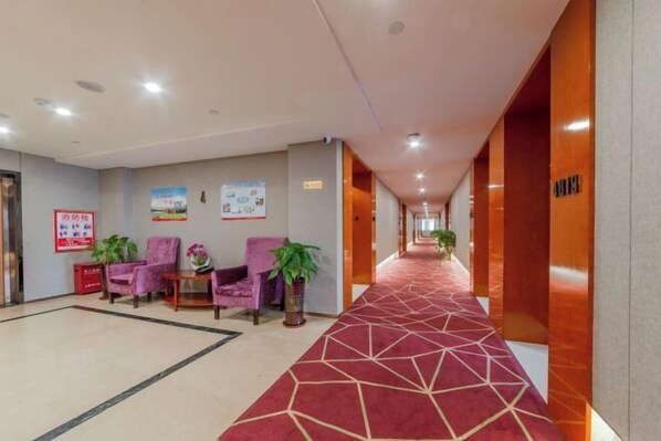 Un hall de hotel con alfombra roja, sillas moradas y plantas en macetas.