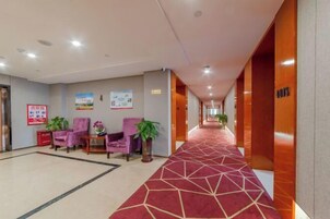 Un hall de hotel con alfombra roja, sillas moradas y plantas en macetas.