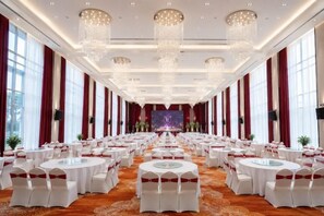 Une salle de banquet avec des tables rondes, des lustres et une scène à l’avant.