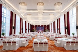 Un salón de banquetes con mesas redondas, candelabros y un escenario al frente.