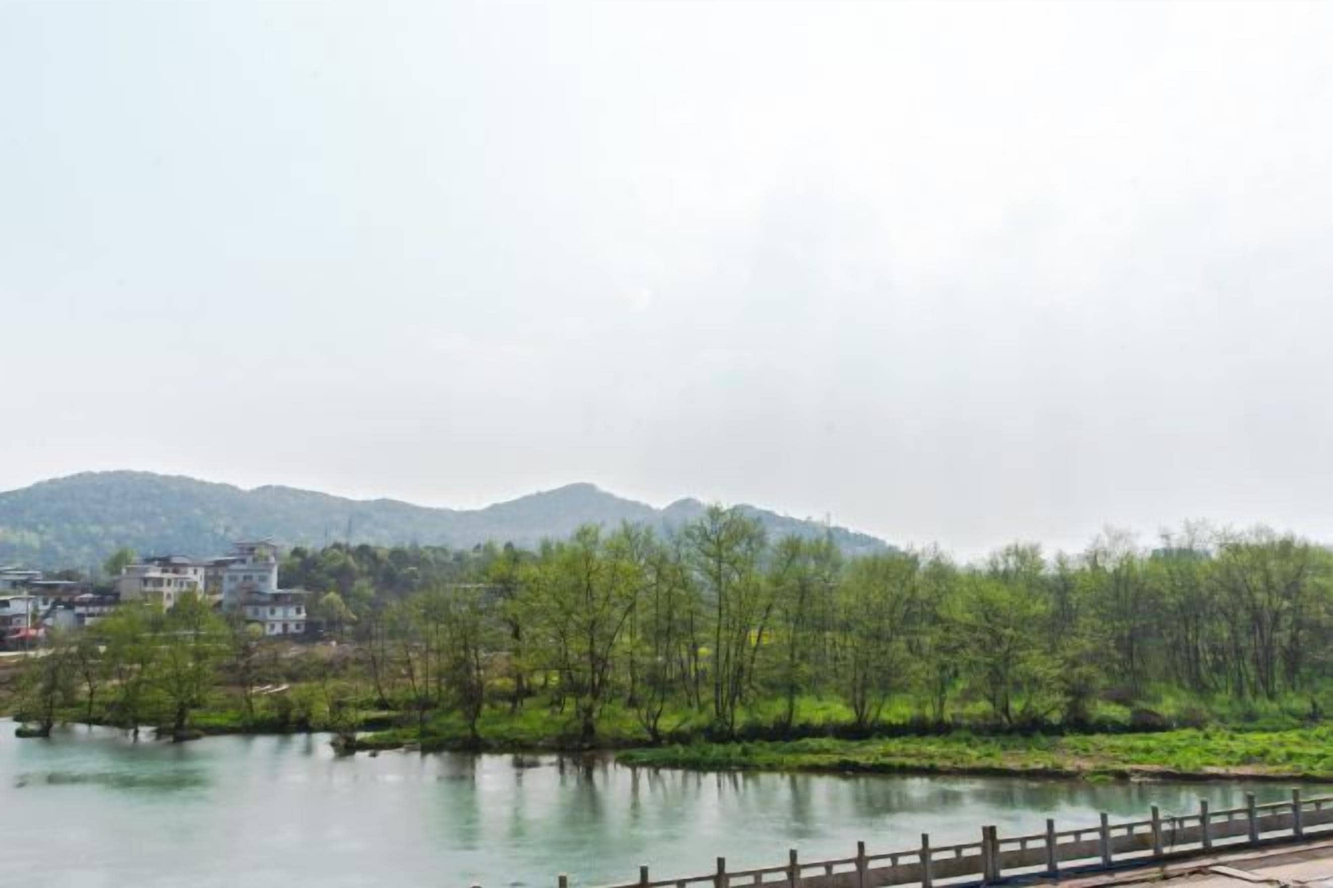 A river with a wooden bridge, surrounded by greenery and buildings in the background.