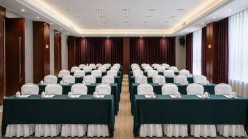 Ein Konferenzraum mit Tischen in Reihen, jeweils mit weißem Tischtuch und weißer Tischläufer.