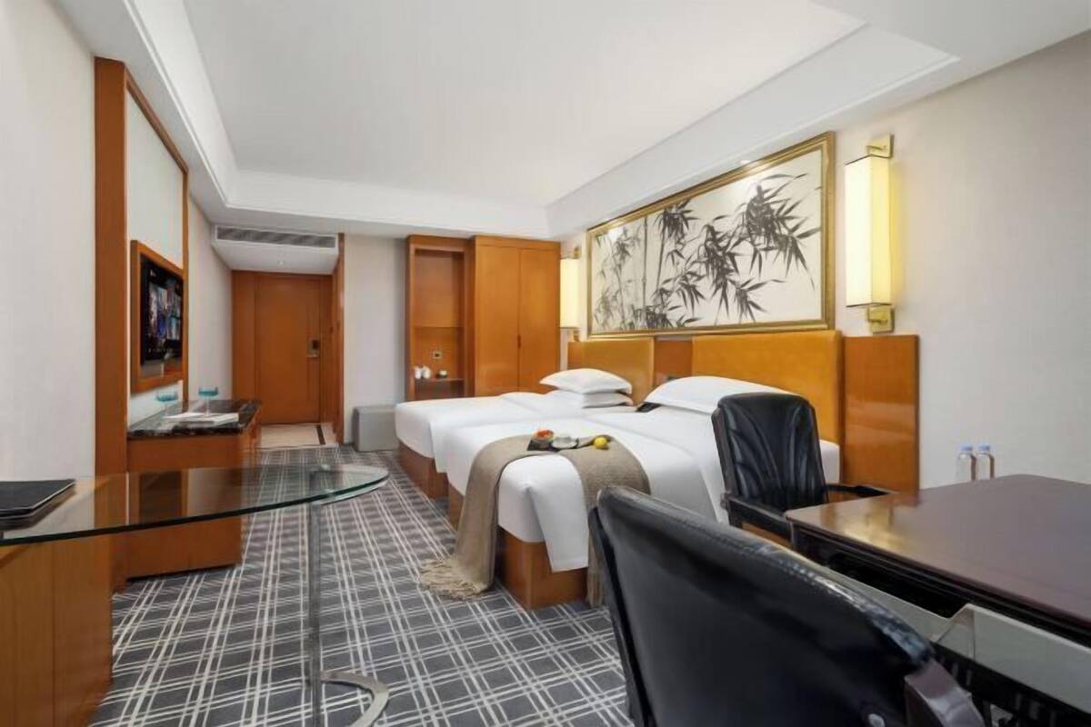 A hotel room with two beds, a desk, a chair, a glass table, and a large painting on the wall.