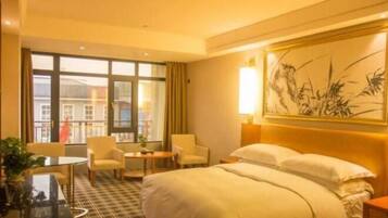 Habitación de hotel con una cama grande, dos sillones, una mesita y vistas a edificios a través de la ventana.