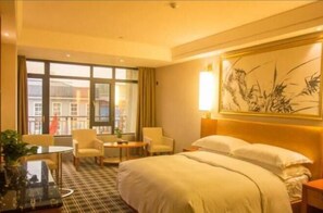 Habitación de hotel con una cama grande, dos sillones, una mesita y vistas a edificios a través de la ventana.
