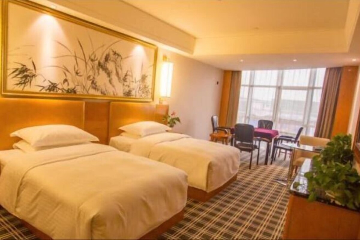 Habitación de hotel con dos camas, un ventanal grande, un cuadro en la pared y una pequeña mesa con sillas.