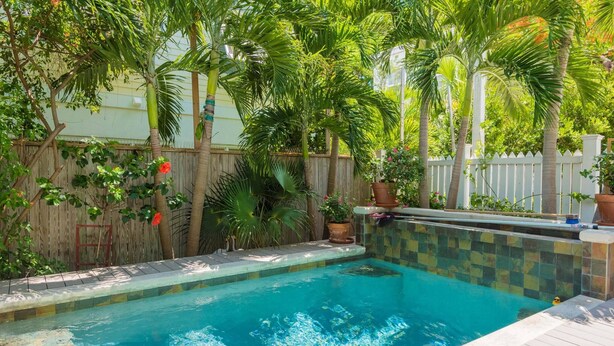 A swimming pool with a tiled edge, surrounded by a wooden fence and lush greenery. - Ecco Domani by AvantStay | Gorgeous Home w/ Pool, Balcony in Great Location (Key West)