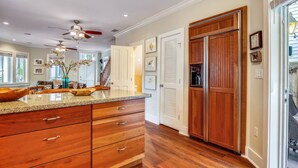 A kitchen with wooden cabinets, granite countertops, and a ceiling fan. - Ecco Domani by AvantStay | Gorgeous Home w/ Pool, Balcony in Great Location (Key West)